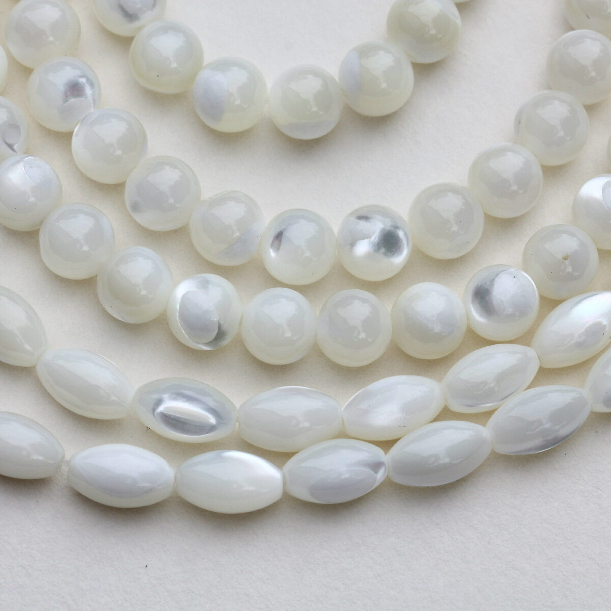 Close-up of white mother-of-pearl beads in round and oval shapes, arranged on a light background for jewellery making