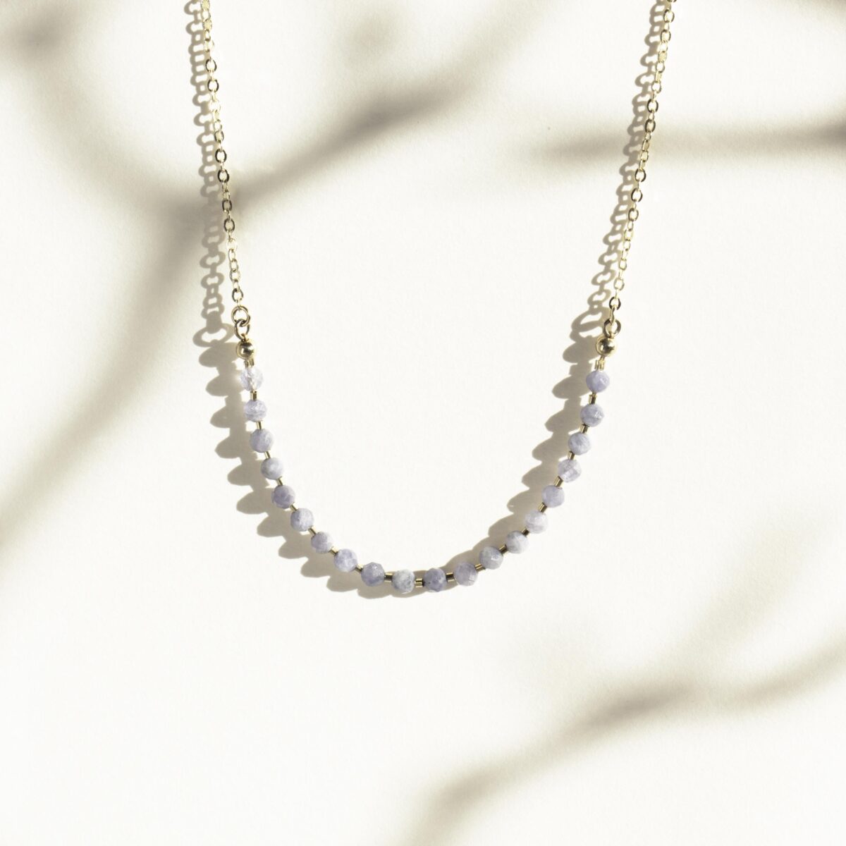 Handcrafted gold chain necklace with faceted Iolite gemstone beads photographed in soft natural light with shadow play