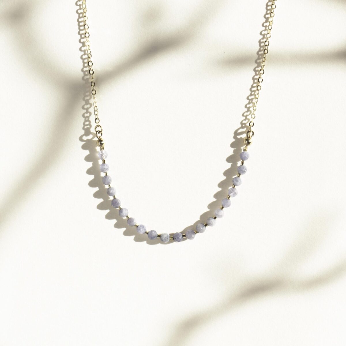 Handcrafted gold chain necklace with faceted Iolite gemstone beads photographed in soft natural light with shadow play