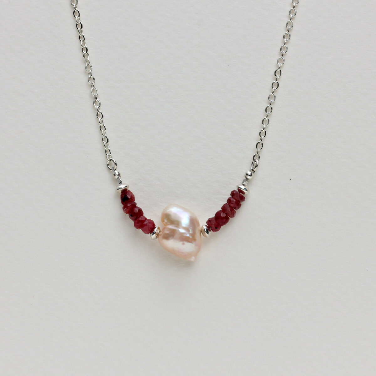 Heart-shaped pearl and ruby necklace on a sterling silver chain, featuring deep red ruby beads and a unique natural pearl symbolizing eternal love and elegance