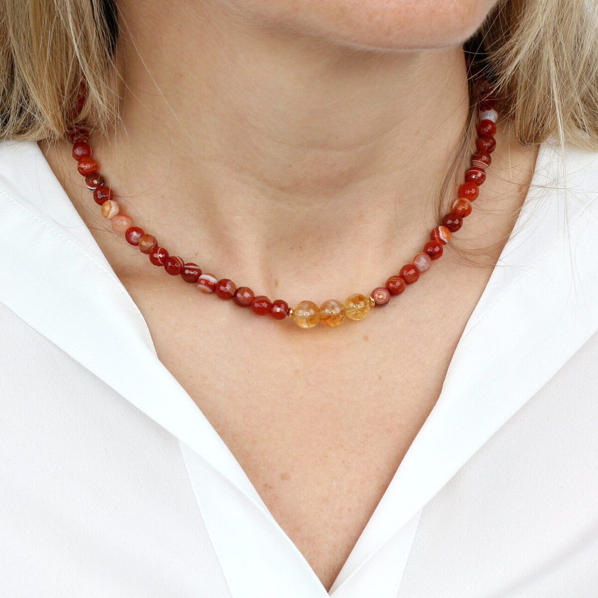 Close-up of a woman wearing a Carnelian and Citrine bead necklace, showcasing warm red and golden hues that promote vitality, joy, and confidence.