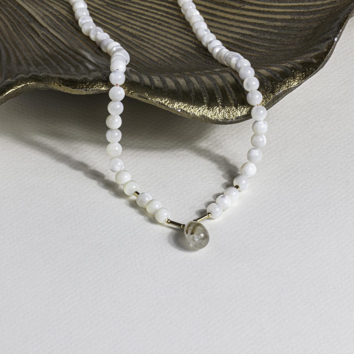 Golden Rutilated Quartz and Mother of Pearl necklace resting on a gold-edged shell, styled on a neutral background to evoke calm and serenity