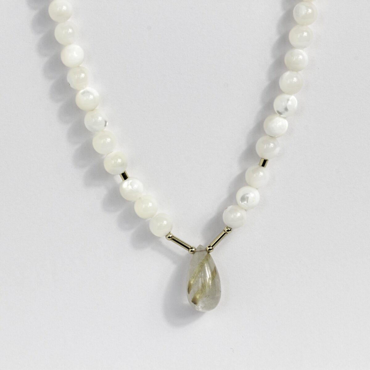 Close-up of golden rutilated quartz and mother of pearl beads on silk thread, highlighting 14K gold-filled clasp craftsmanship