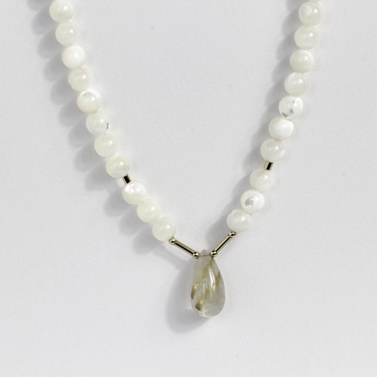 Close-up of golden rutilated quartz and mother of pearl beads on silk thread, highlighting 14K gold-filled clasp craftsmanship