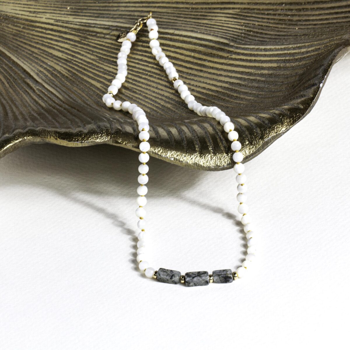 Elegant Mother of Pearl and Tourmaline Quartz necklace with gold-filled clasp, displayed on a textured bronze dish over a white surface