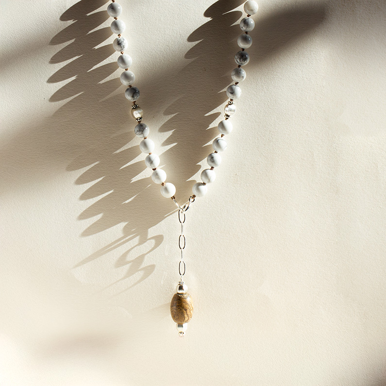 Earthbound Strength Necklace with howlite beads and jade pendant casting soft shadows on beige background