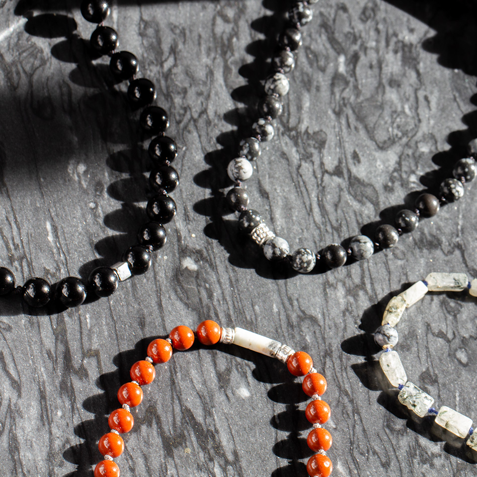 Artisan men’s gemstone necklaces with red jasper, obsidian, and sterling silver accents on marble surface