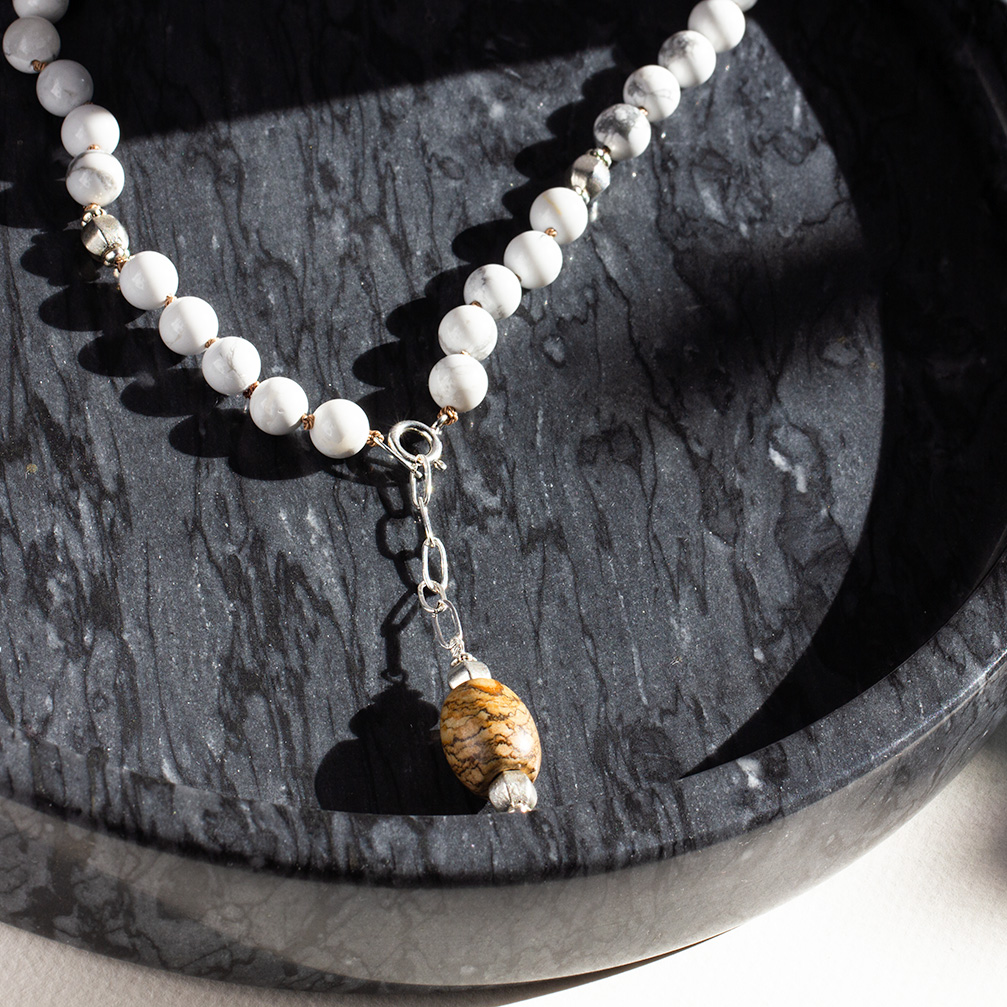 Close-up of men’s howlite jade strength necklace with sterling silver chain and brown jade pendant on marble background.