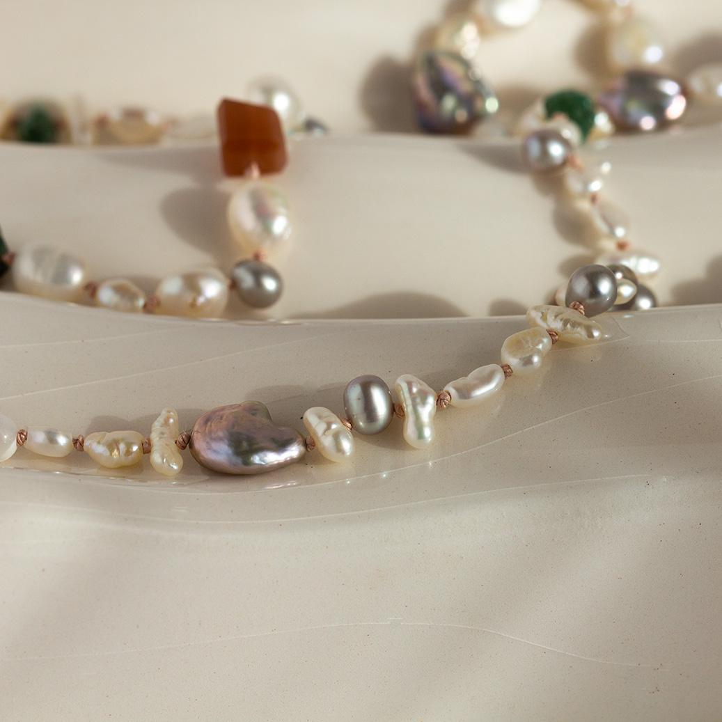 Close-up of Soft Radiance Pearl Emerald Necklace showing mixed grey, white, and creamy pearls with green emeralds on pink silk thread, highlighting the natural shimmer and 9K gold details