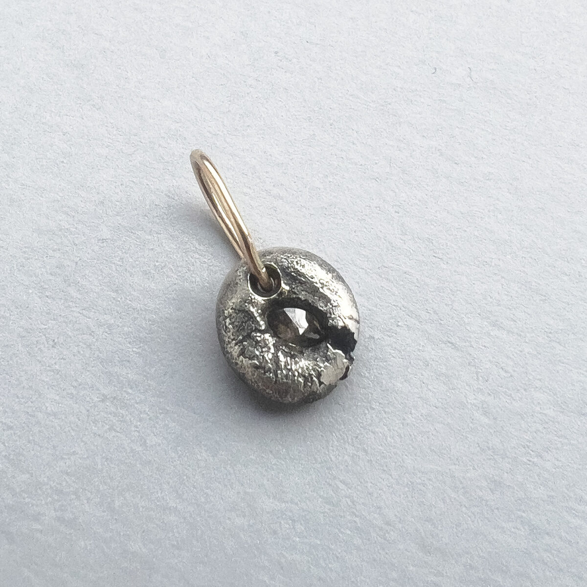 Round textured silver pendant with a dark central fissure and a slim 9ct gold bail on a light background.