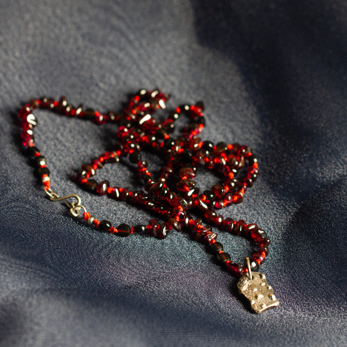Amonta Kin Ancestral Roots red garnet and black spinel necklace with oxidised sterling silver pendant, hand knotted on vivid red silk.