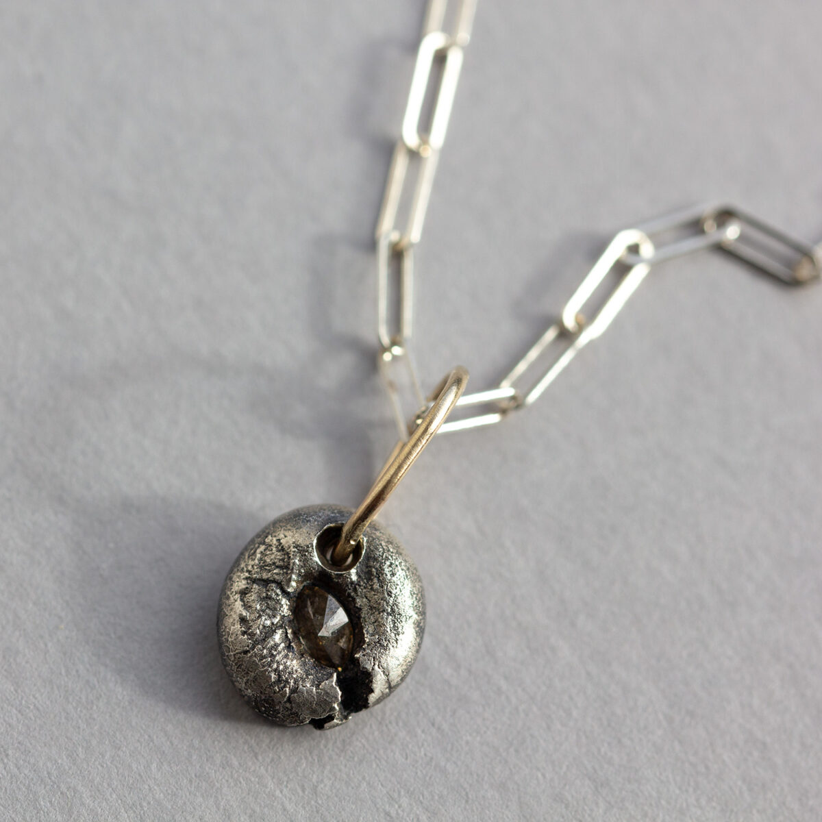 Oxidised silver donut-shaped pendant with marquise salt and pepper diamond and gold bail on a sterling silver paperclip chain.