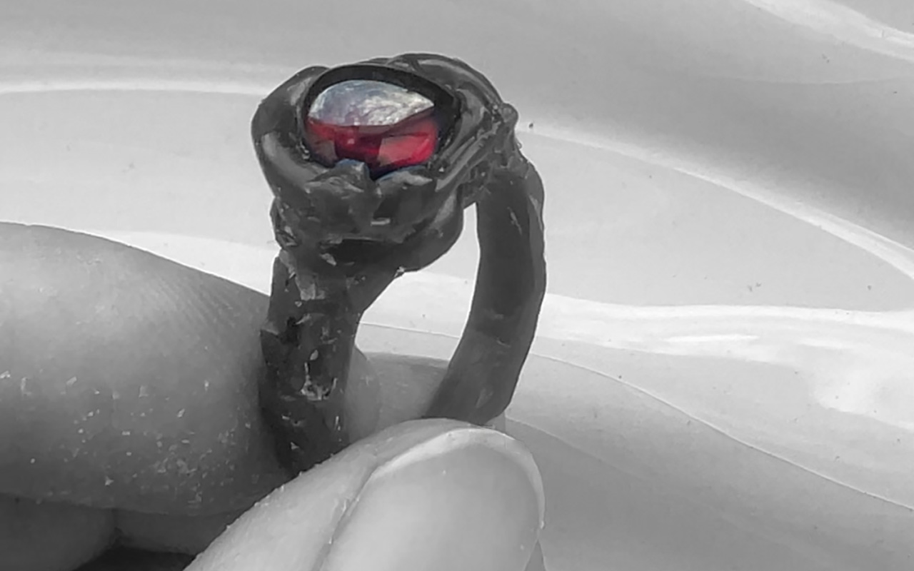 Hand holding a sculptural wax ring model with a red garnet positioned in the setting