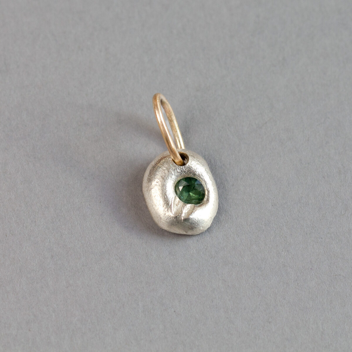 Forest green sapphire pendant in textured Argentium silver with a 9ct gold bail, photographed on grey paper.